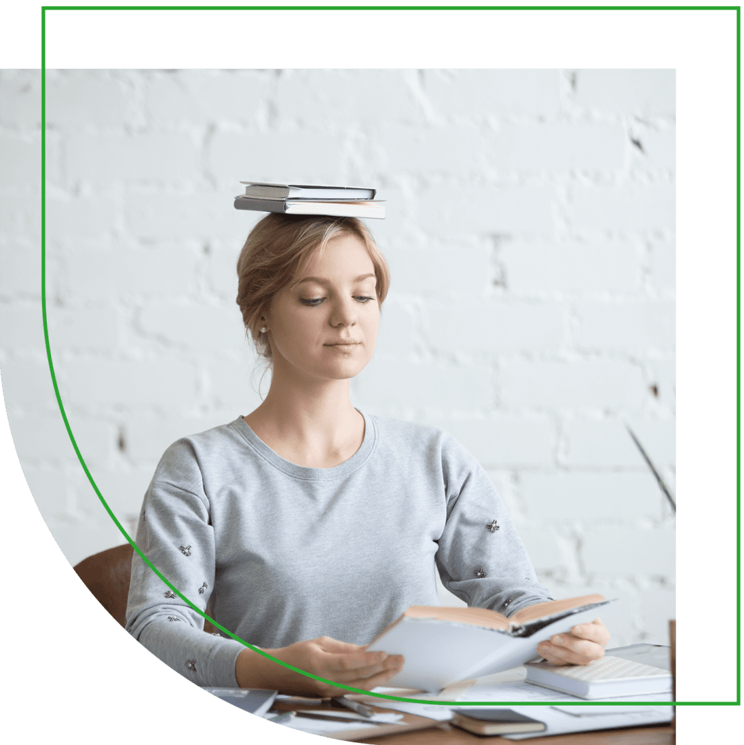 A woman sitting at a table with papers and a book on her head.