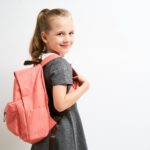 A girl with a backpack is smiling for the camera.