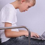 A boy is sitting on the floor using his laptop.