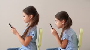 A girl sitting in front of a wall holding a cell phone.