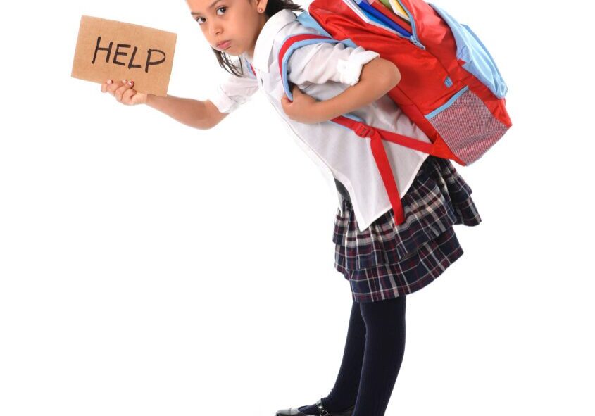 A girl in school uniform holding a sign and backpack.